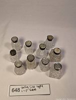 Overview photo of 10 small salt and pepper shakers with clear cut glass bodies and silver tops.