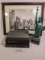 Framed photo of the New York City skyline including Twin Towers, two hardcover books, and Statue of Liberty figurine in front.