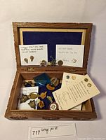 Wooden box with blue fabric lining containing a collection of vintage pins, some notes detailing the pins included.
