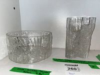 Oiva Toikka Flora bowl and Tapio Wirkkala Pinus Avena vase shown side by side on a shelf with labels.