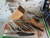 Wooden knife block with assorted knives laid out next to plastic cutting board