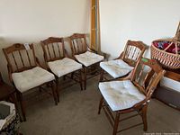 Five wooden dining chairs arranged in a corner with white padded cushions on the cane seats.
