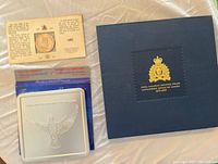 Collection of items including blue folder with gold emblem, silver-tone case with bird emblem, and coin with certificate