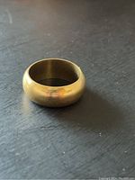 Front three-quarter view of the domed gold band resting on a dark surface.