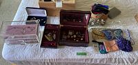 Wide view of wood jewelry box, lucite box, multiple small pouches and costume jewelry pieces displayed on a table.