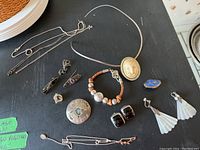 Full view of all jewelry items including earrings, necklaces, bracelets, pins, and chains placed on black surface.