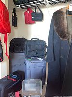 Photo showing large black Tossa suitcases stacked, black laptop bag, smaller bags hanging from shelf, and part of a coat.