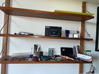 Photo showing shelves with the Panasonic CD player, cassette recorder, Cross pen box and multiple pocket cutters and pins arranged on wood shelf.