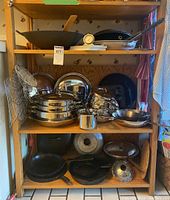Top shelf showing large carbon steel wok, wooden spatula, metal thermometer and a stainless steel frying pan