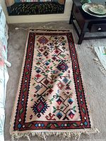 Full view of one decorative patterned rug on carpeted floor near furniture.