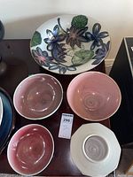 Four signed pottery items displayed, including a large floral bowl and three pink glazed bowls, one with exterior painted landscape.