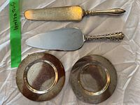Two round sterling silver plates with tarnishing, alongside two sterling servers with different blade shapes and handle designs spread on a fabric surface.