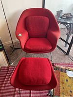 Full view of red womb chair and matching footstool on striped rug