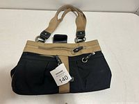 The exterior of the women's purse showing beige and black colors, handles, and front zippered compartments.