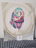 Frontal view of colorful stylized portrait featuring a person wearing a gas mask with abstract swirled shapes for hair, on a canvas board with light background marks.