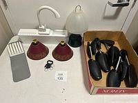 Photo of assorted household items including two red lampshades, a small lamp with frosted glass dome, gray massager, black keychain, and black shoe stretchers in a cardboard box.