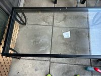 Top view of the glass coffee table showing clear tempered glass and black metal frame on a tiled floor.