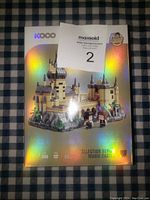 Photo of KOCO Magic Castle building block set box showing the assembled castle with two small figures and holographic finish.