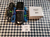 Photo showing the telephone handset, cords bundled with rubber bands, and a white sealed ink cartridge box on checkered fabric.