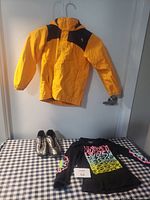 Yellow and black jacket hanging, colorful shirt and soccer cleats on checkered surface
