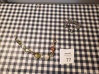 Top view showing the multicolored gemstone necklace laid flat and matching silver-tone bracelet on checked cloth background
