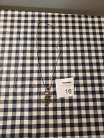 Full view of the owl necklace with chain on blue and white checkered fabric.