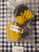 Three yellow and black bristle drill attachment brushes sealed in a clear plastic bag on a blue and white checkered cloth