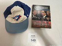 Front view of blue and cream vintage Toronto Blue Jays baseball cap with embroidered logo next to Law & Order Season 14 DVD box set.