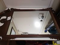 Front view of vintage wall mirror showing the dark wooden carved frame and reflective glass surface.