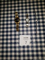 Four wrist watches laid flat on blue and white checkered fabric, showing front face and bands.