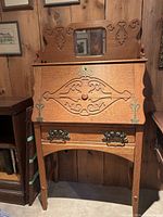 Full front view of antique secretary desk showing carved wood details, brass pulls, mirror, and fold-down panel closed