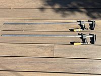 Two 36-inch metal bar clamps laid out horizontally on a wooden surface, showing full length and condition