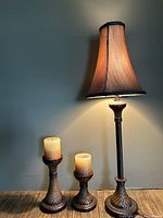 Full view of the table lamp lit with the two candle holders on a wooden surface against a plain wall.
