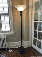 Full view of the black and brown metal floor lamp standing near a window and glass door, showing its height and overall design.