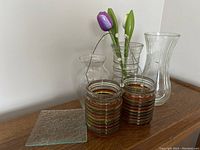 View of the three glass vases, square trinket dish, and artificial purple flowers arranged on a wooden surface