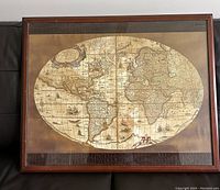 Photo showing framed vintage style world map desk pad with wooden border and glass top, resting on a dark leather surface.
