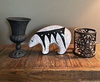 Two cast iron candle holders, ceramic bear sculpture, and small decorative goblet shown together on wood surface