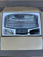 Opened box showing the heater unit inside styrofoam packaging with attached power cord and included mounting hardware.