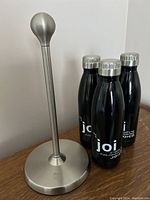 Full view of Umbra stainless steel paper towel holder next to three black promotional steel water bottles with silver caps