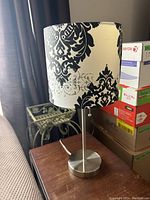 Table lamp on wooden surface with black and white decorative shade showing minor seam separation.