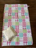 Full view of the Tommy Hilfiger quilt laid flat on the floor with the beige quilted pillow placed on top showing the colorful patchwork pattern on the quilt.