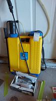 Yellow Power Fist back pack sprayer with pump handle and attached spray wand, showing measurement markings up to 16 liters