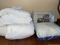 Full/queen white quilt and matching shams with bamboo pillow packaged in plastic, sitting on floor near wall outlet