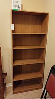 Full view of the manufactured wood bookcase with five shelves in light oak finish.