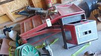 Image showing two red metal vehicle ramps, a red and black rolling stool, and a green hose reel in garage setting