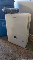 White Danby Premiere branded dehumidifier with a black cylindrical filter wrapped in plastic placed on top, standing on carpet.