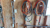 Multiple extension cords hanging on hooks, black and orange in color, one with attached work light.