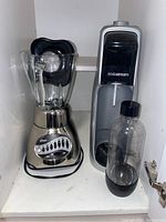 Oster 16-speed blender and SodaStream soda maker with refill bottle on shelf.