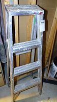 Front view of the 4-foot aluminum step ladder showing multiple paint splatters and scratches on steps and sides.