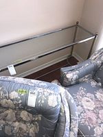 Console table with beveled glass top placed against wall flanked by floral upholstered chairs.